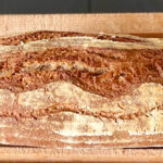 Fertig gebackenes längliches Brot auf einem Hlzgitterbrett.