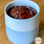 Ein dunkelbrauner Kuchen in einem weißen Becher. Die untere Hälfte des Bechers ist mit hellblauen Silikon ummantelt.
